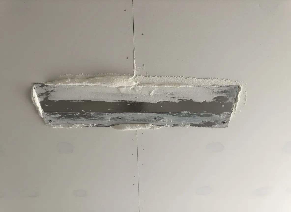A taped ceiling joint worked overhead, the knife drawing compound along a seam between two sheets