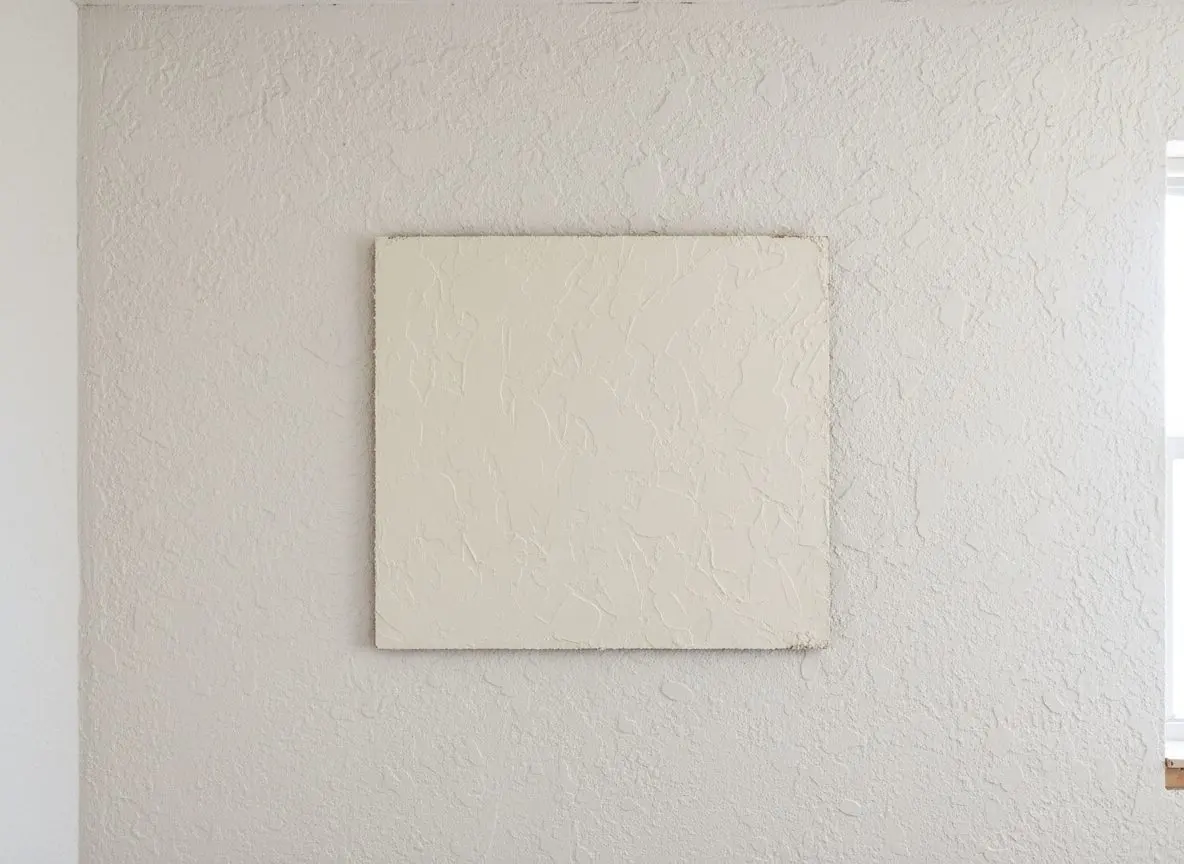 A dried sample board of sprayed knockdown held flat against an existing textured wall, close and square on